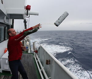 Scientist throws a small sonobuoy over the side of the ship.