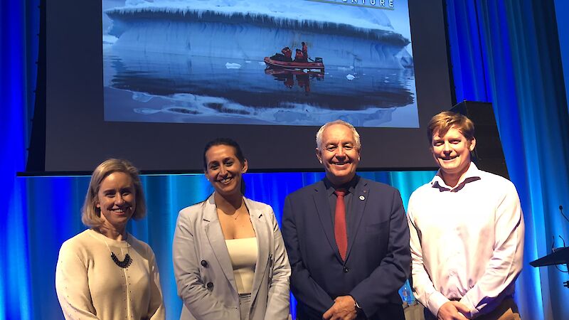Four people posing before a screen displaying title ‘The Antarctica Experience'.