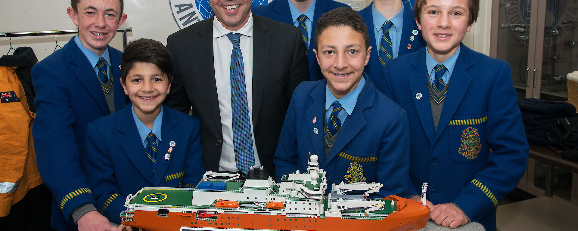A group of six secondary school students with the Environment Minister standing around a model of the new Antarctic icebreaker.