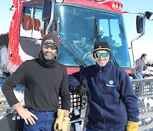 Two men standing in front of a traverse tractor.