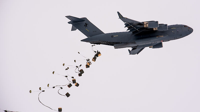 Pallets of supplies attached to parachutes drop from the tail end of a C-17A aircraft.