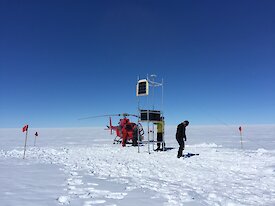 Scientists installing equipment on the Totten Glacier with a red helicopter in the background.