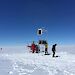 Scientists installing equipment on the Totten Glacier with a red helicopter in the background.
