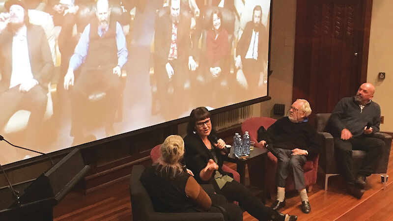 People sitting in conversation on a stage, with a projected image of Antarctic expeditioners behind.