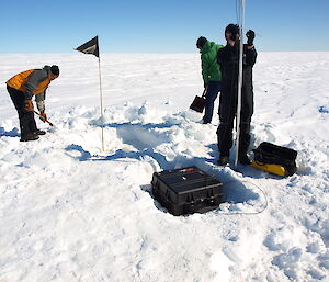 A team deploy an ApRES instrument (inside the black box) on the Sørsdal Glacier near Davis in the 2015–16 summer. The radar instrument is buried in a shallow pit under the ice. It sends a radio pulse down through the ice to measure its thickness with millimetre accuracy.