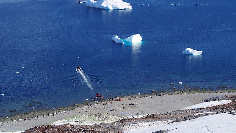 Tourists disembarking from a ship and climbing a snow-covered slope.