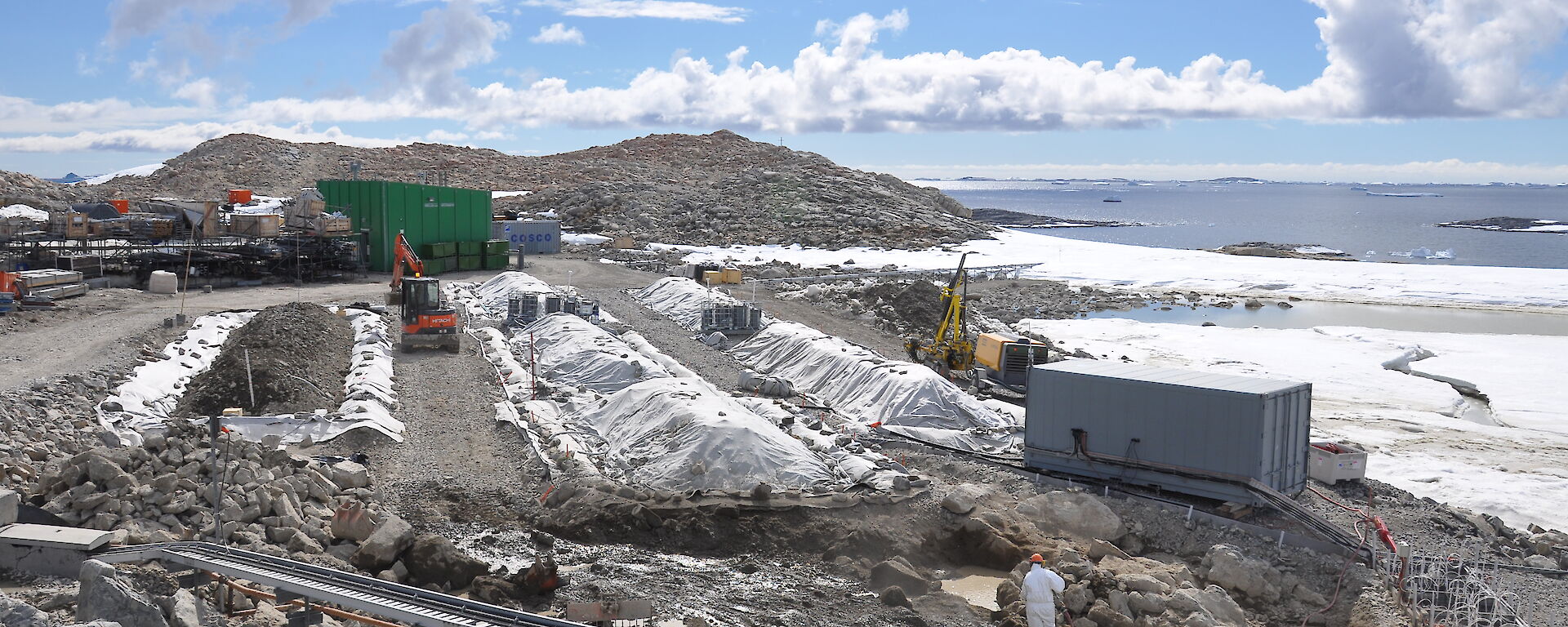 Remediation at the Main Power House fuel spill site. Contaminated soil is being excavated in front of the permeable reactive barrier (lower right of photo) and placed into biopile 6. Biopiles 1–5 can be seen with their covers on. Aeration systems are visible between the biopiles.