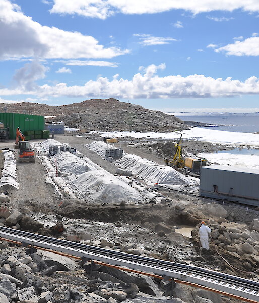 Remediation at the Main Power House fuel spill site. Contaminated soil is being excavated in front of the permeable reactive barrier (lower right of photo) and placed into biopile 6. Biopiles 1–5 can be seen with their covers on. Aeration systems are visible between the biopiles.