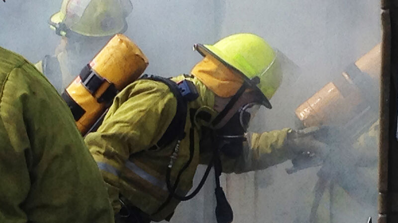 Expeditioners practice using breathing equipment as they enter a burning building.