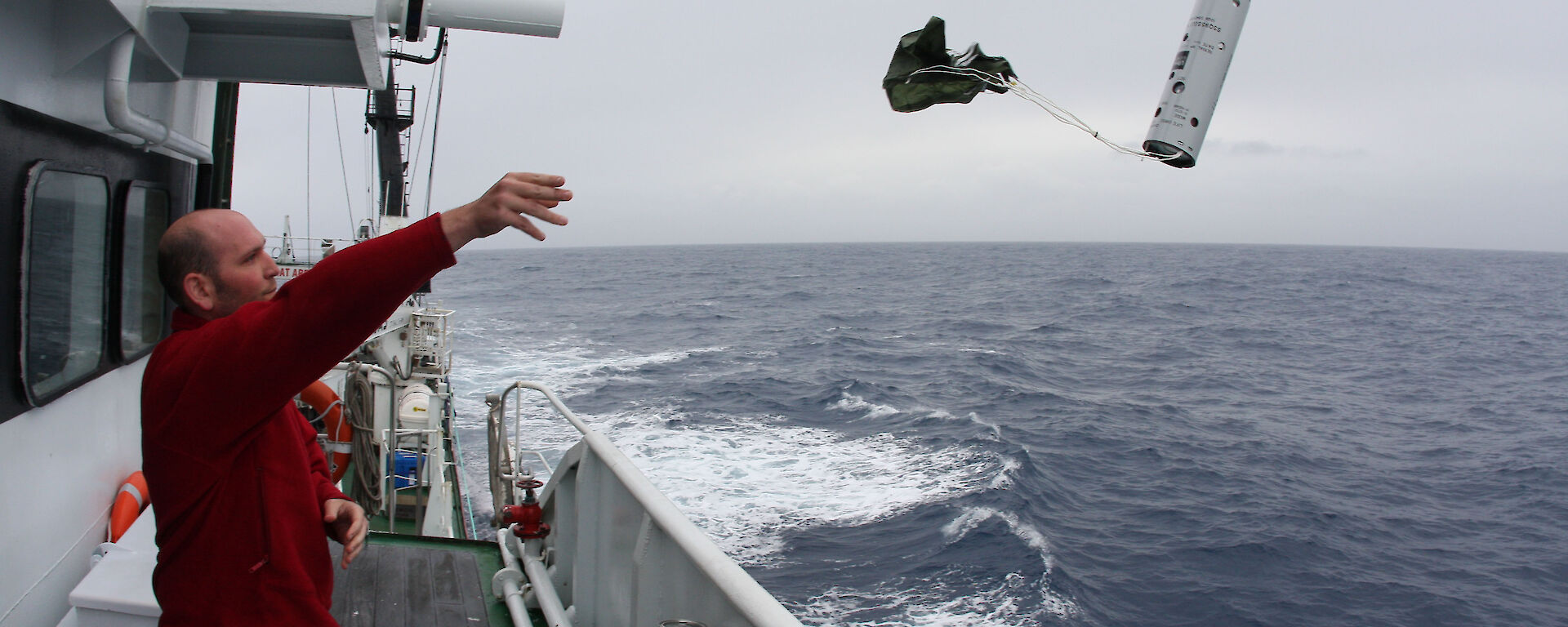 Acoustician Dr Brian Miller throws a sonobuoy into the ocean from the side of the ship