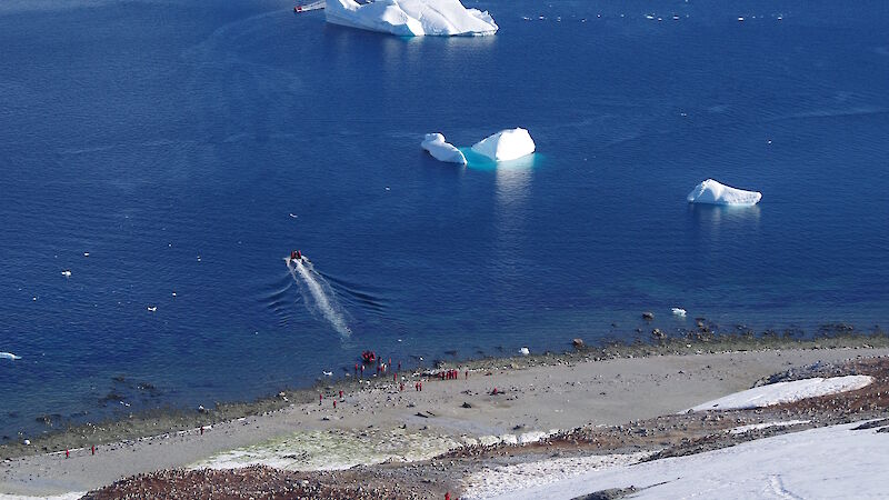 A French cruise ship off the coast of Danco Island on the Antarctic Peninsula with tourists climbing a snow-covered slope in the foreground