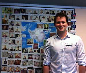 Medical student John Cherry standing in front of a pin-board of photos of Antarctic doctors