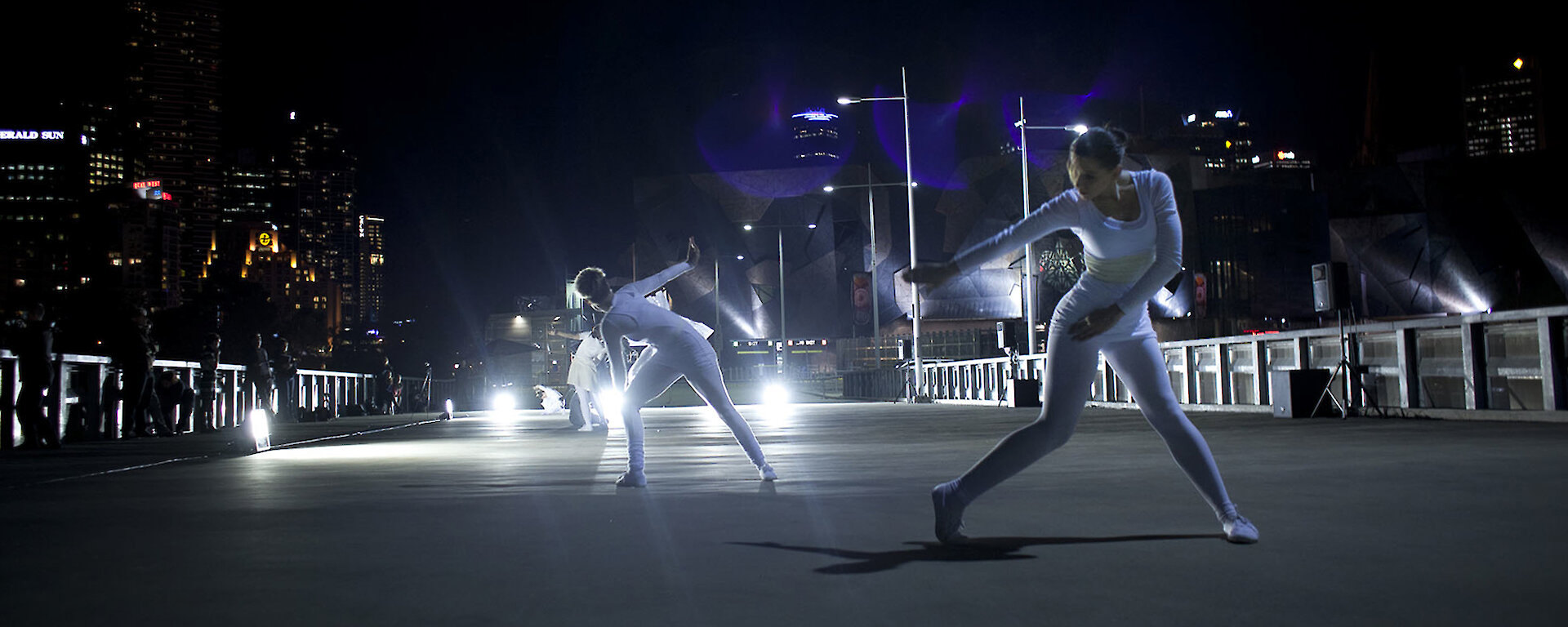 Dancers dressed in white perform ‘Polarity’ in Melbourne’s Federation Square under dramatic lighting