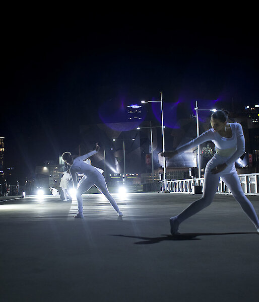 Dancers dressed in white perform ‘Polarity’ in Melbourne’s Federation Square under dramatic lighting