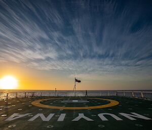 A giant sun on the horizon, photographed from the green helideck of a ship.