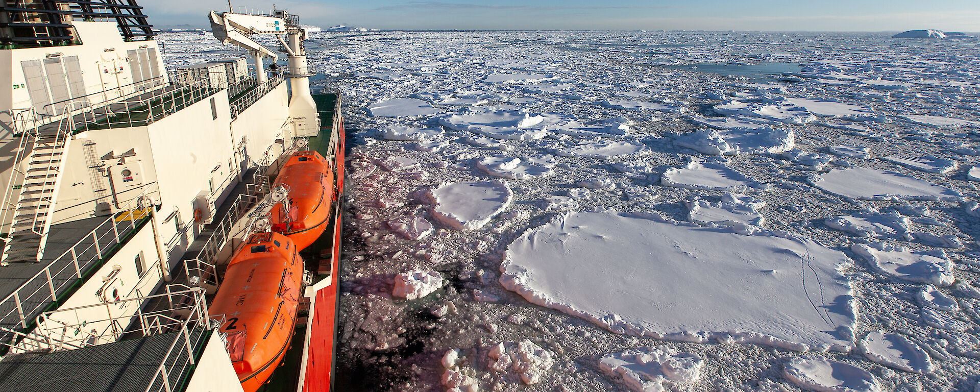 An orange and white ship sails through floating chunks of ice.