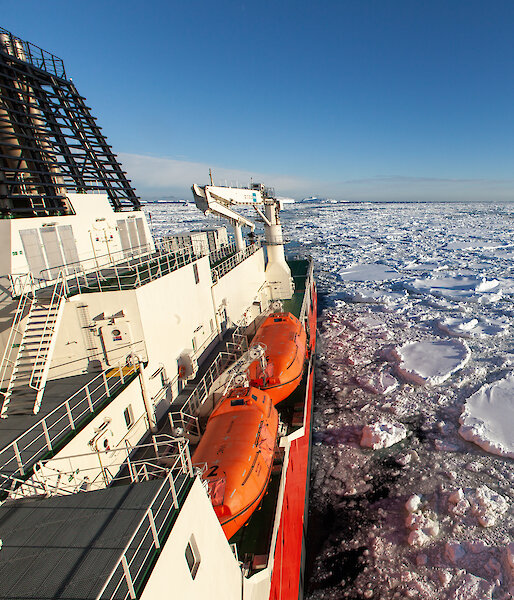 An orange and white ship sails through floating chunks of ice.