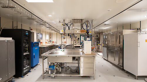 A brightly lit room contains sinks, desks, cabinets and scientific equipment.