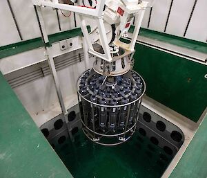 A large cylinder containing many capsules is lowered into a pool.
