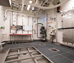 An empty room with a steel mesh floor and pipes waiting to be connected to water processing equipment.