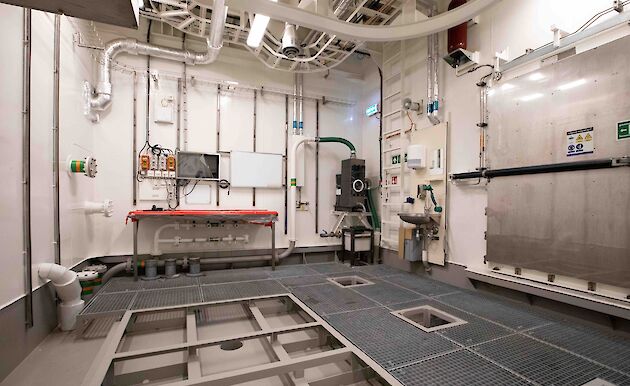 An empty room with a steel mesh floor and pipes waiting to be connected to water processing equipment.