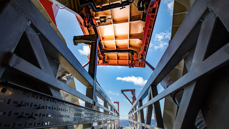 An orange door opens to reveal the sea and the sky. A metal walkway in the foreground is ready to be extended out of the open door.