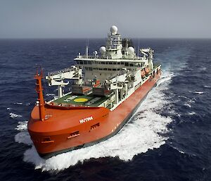 Aerial view of the bow of Nuyina in the Atlantic Ocean, with waves spraying up either side.