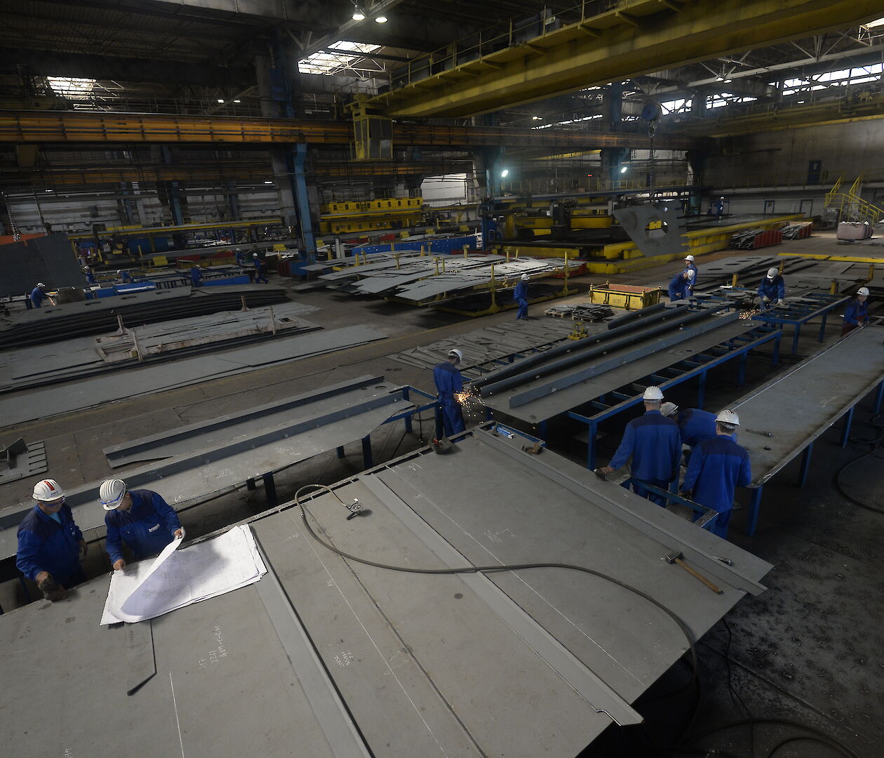 Workers in a large shed with big pieces of steel