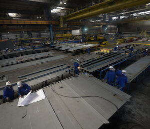 Workers in a large shed with big pieces of steel