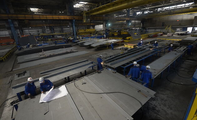 Workers in a large shed with big pieces of steel