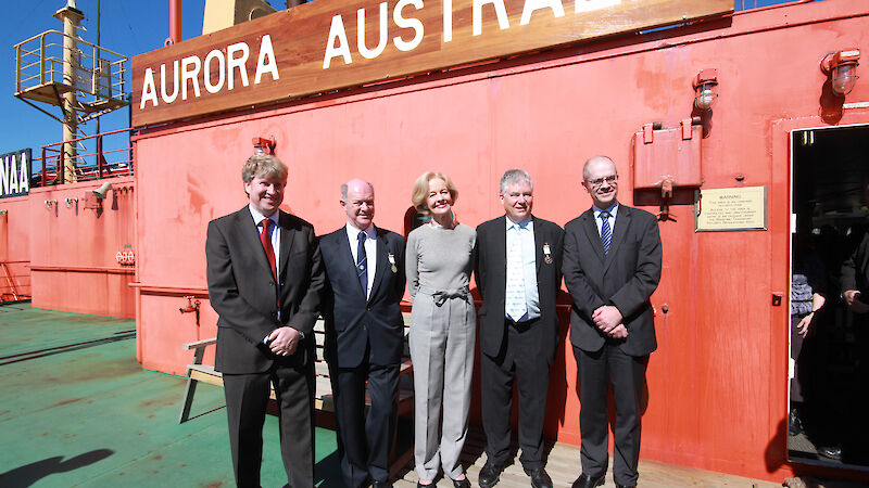 A group stands in front of a ship at the wharf.