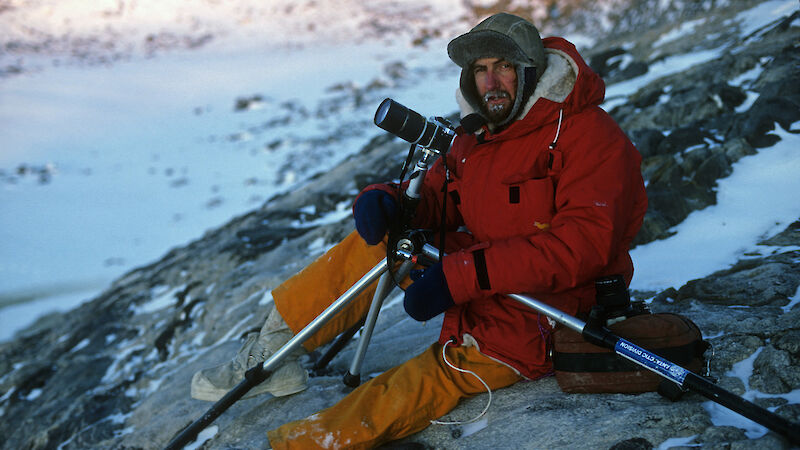 Scientist sitting on a rocky slope with camera and tripod