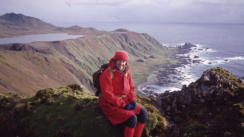 Scientist sitting on a rock at top of cliff with bay in background