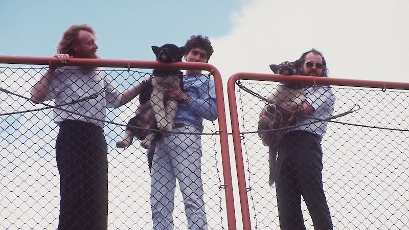 Three expeditioners holding husky dog puppies on the deck of ship