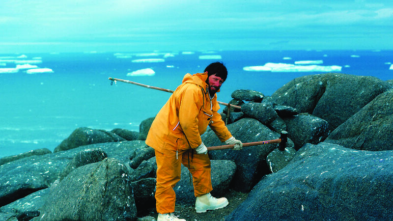 Scientist with mallet bending over rocks