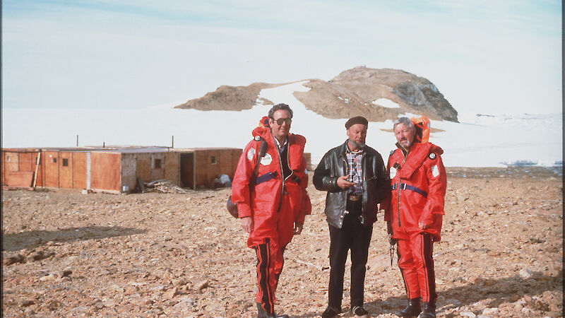 Australian expeditioners standing with Russian expeditioner. Low building behind