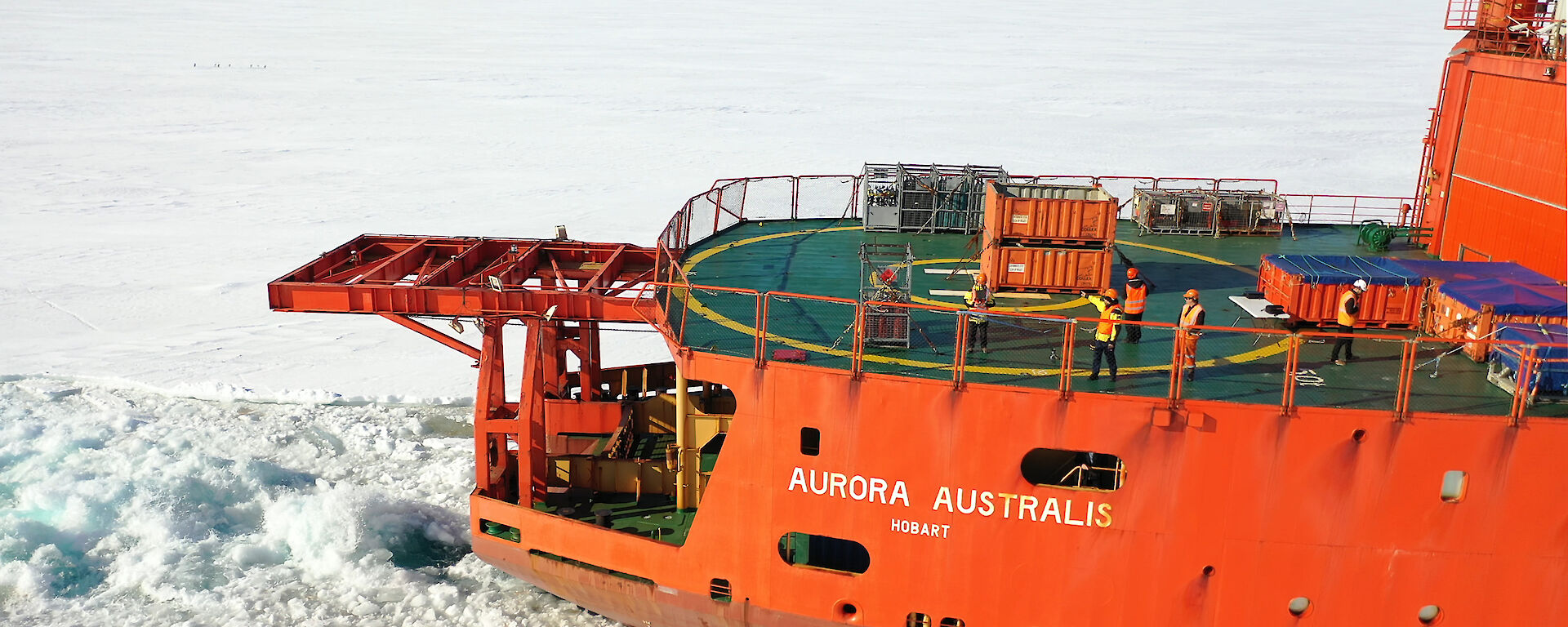 Aerial photograph of an orange icebreaker ship sailing though sea ice.