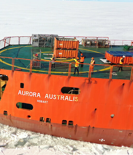 Aerial photograph of an orange icebreaker ship sailing though sea ice.