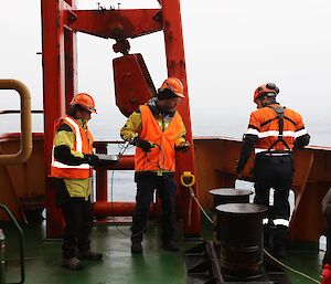 People in hi-vis on the deck of a ship hold recording equipment and a laptop.