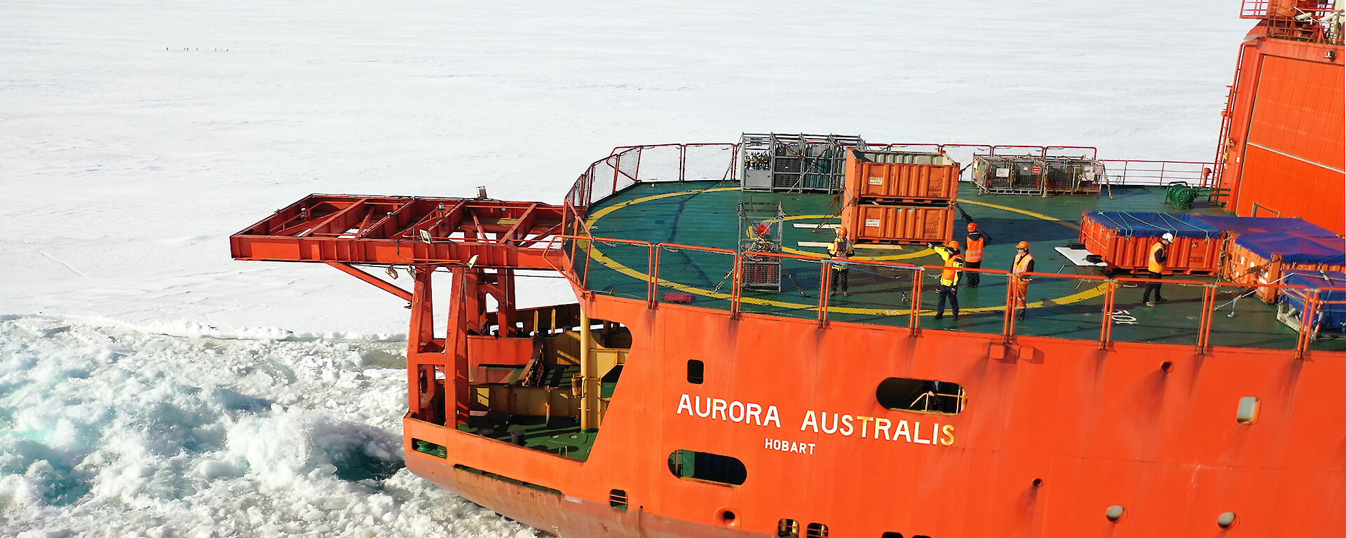 Aerial photograph of an orange icebreaker ship sailing though sea ice.