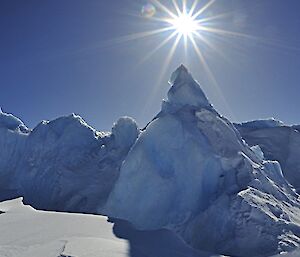 A pyramid shaped iceberg with the bright sun above