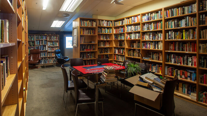 A room with tall bookshelves against all walls, filled with books. A table and chairs are in the middle of the room with a puzzle and more books.