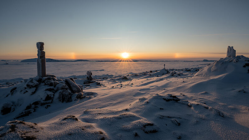 The sun on the horizon and sculptures in a snowy landscape