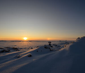 The sun on the horizon and sculptures in a snowy landscape