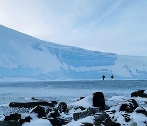 To expeditioners look tiny against a large cliff of ice.