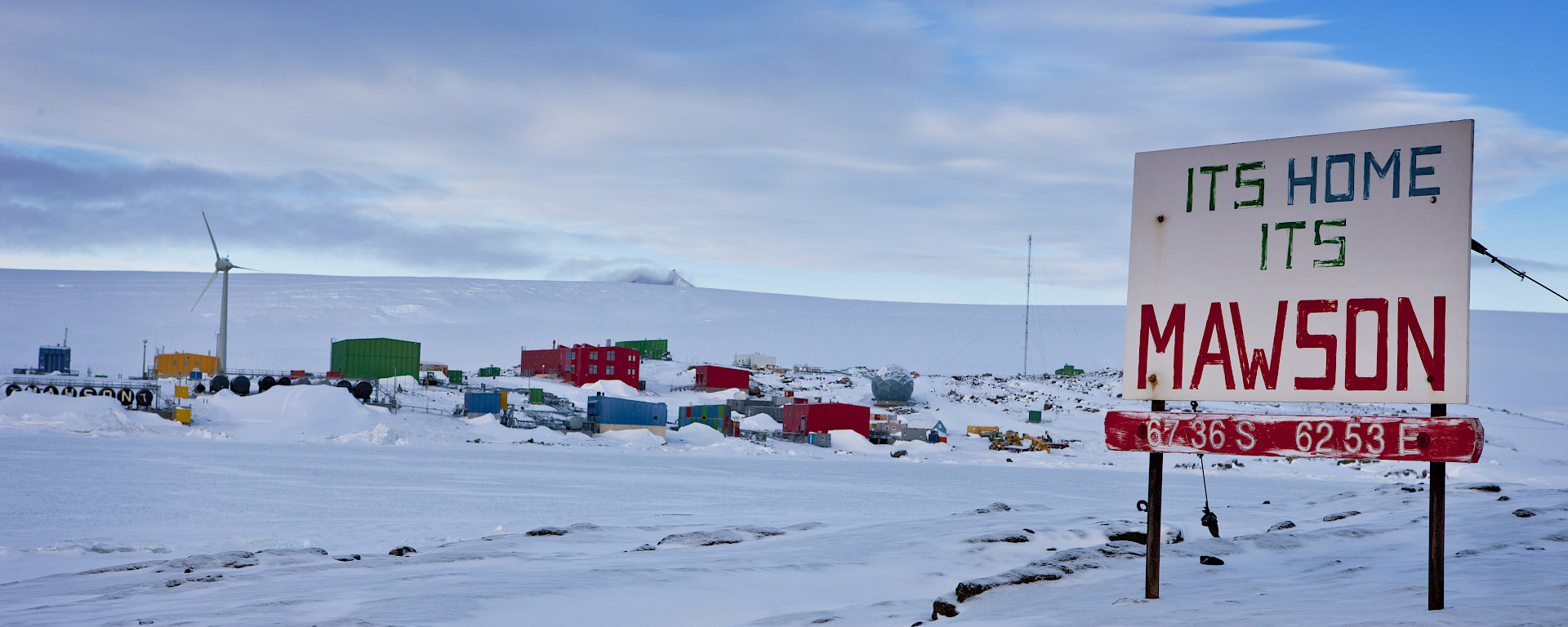 Mawson station from West Arm after snowfall, showing station sign "Its Home its Mawson" plus a iced over Horseshoe Harbour
