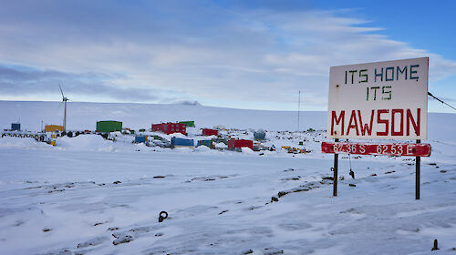 Mawson station from West Arm after snowfall, showing station sign "Its Home its Mawson" plus a iced over Horseshoe Harbour