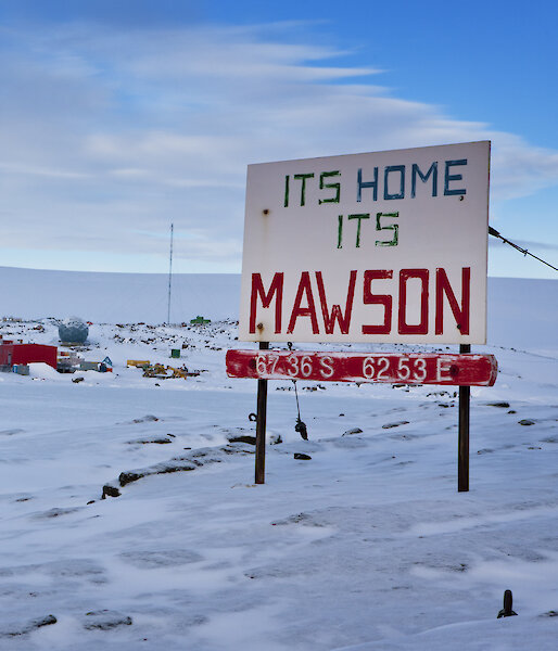 Mawson station from West Arm after snowfall, showing station sign "Its Home its Mawson" plus a iced over Horseshoe Harbour