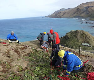 Expeditioners at edge of slope with stretcher attached to ropes