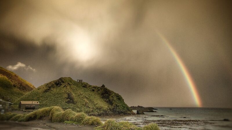 Storm cloud and rainbow over the field hut on a steep green cliff